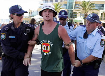 A male youth is arrested on Australia Day 2013 by police. It is believed  he decided to "punch as many people as he could see" after hearing Triple J play 'Mackelmore' in the #1 spot on the Hottest 100